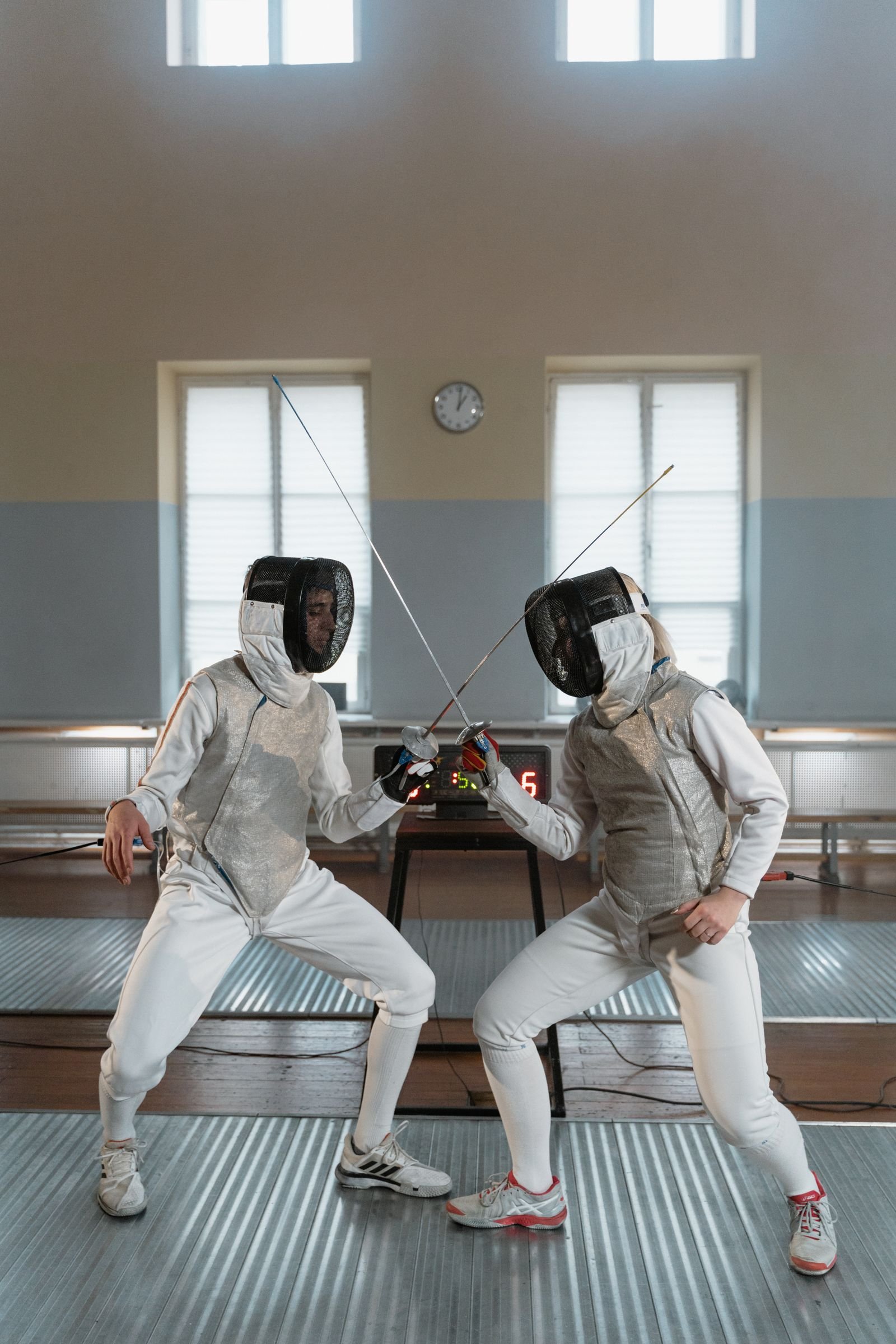 Two fencers facing off in a training hall.