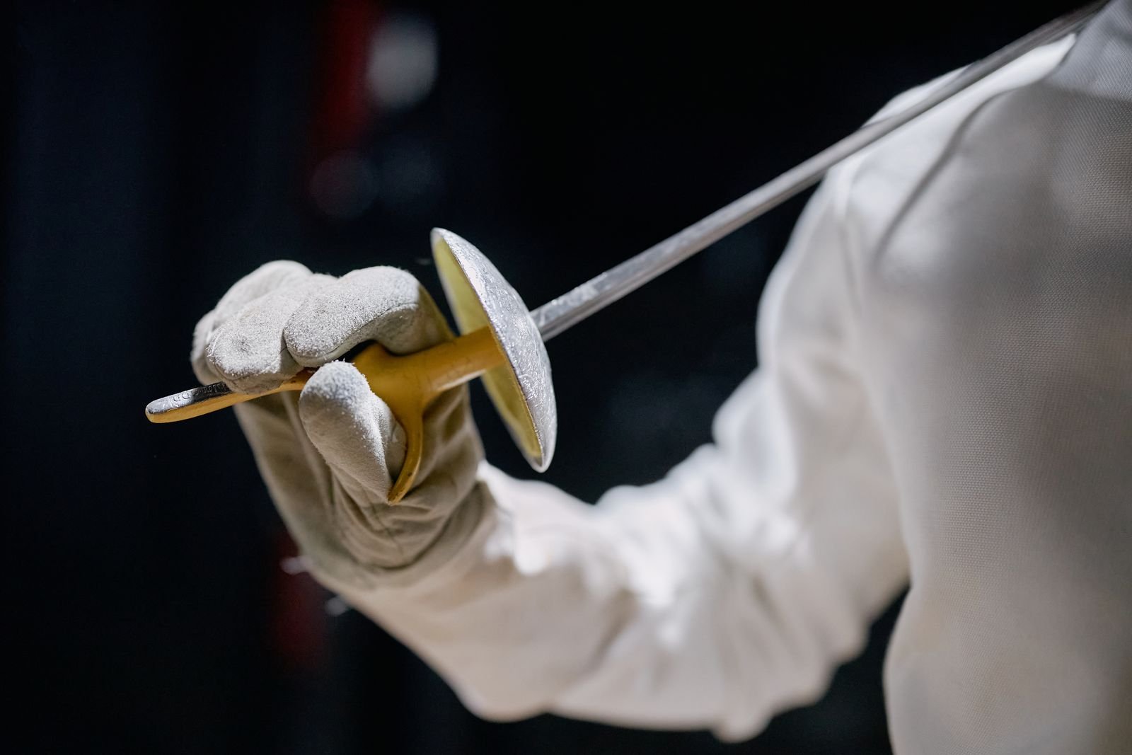 Close-up of a gloved hand gripping the bell-guard of a foil.