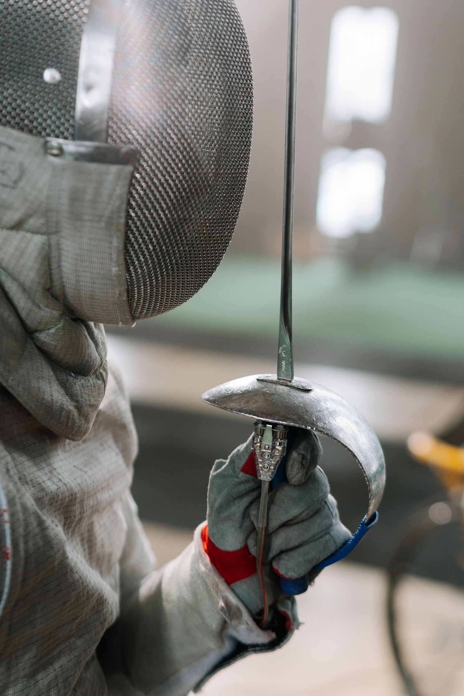 A masked fencer holding a blade in a training hall.